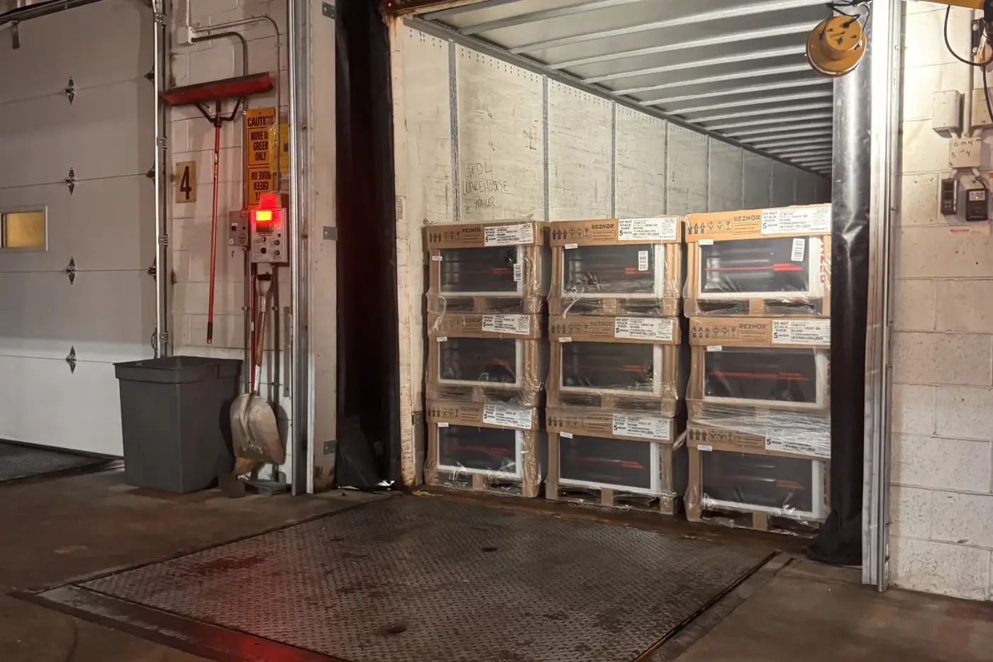 Stacked pallets of shrink-wrapped freight loaded into a 53-foot dry van trailer at a warehouse loading dock.