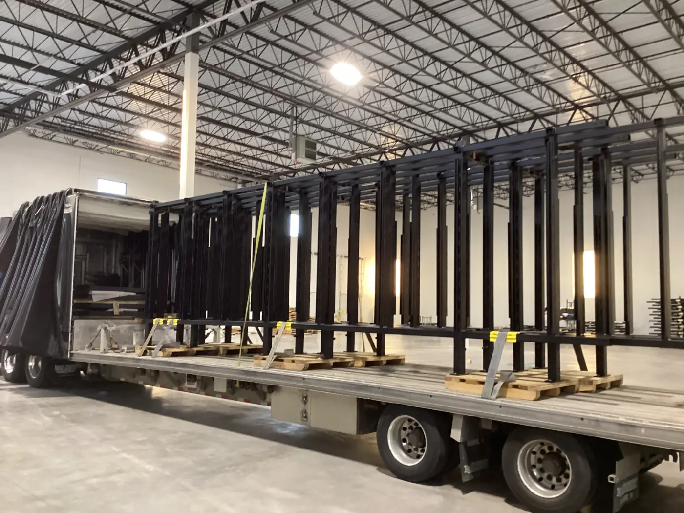 Large industrial freight secured to a step deck Conestoga trailer with the protective curtain retracted inside a warehouse.