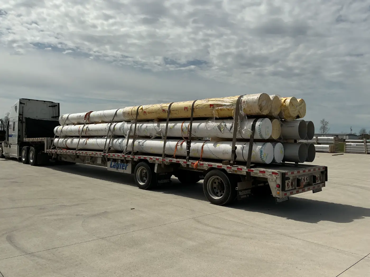 A Laufer step deck trailer loaded with large industrial pipes and freight secured by heavy-duty straps.