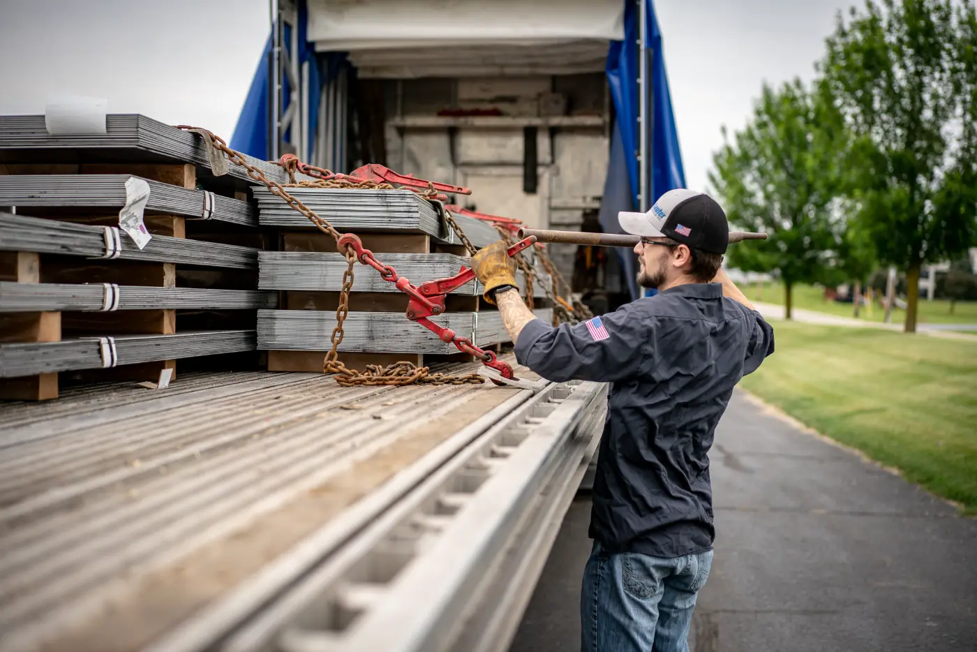 A local flatbed driver secures heavy steel plates with chains and binders on a Laufer Trucking trailer.