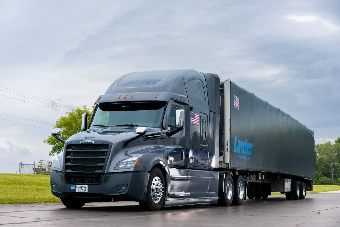 A grey Laufer Trucking Freightliner semi-truck pulls a covered curtain-side flatbed trailer for a regional driver job.