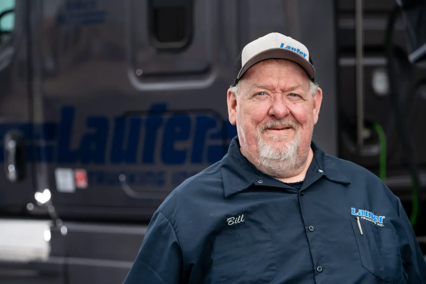 A smiling Laufer Trucking regional dry van driver standing in front of his semi-truck.