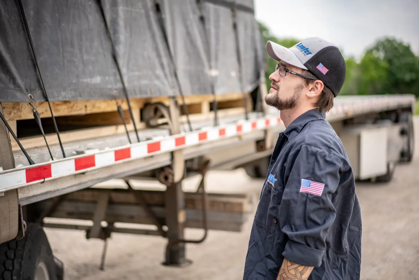 A professional truck driver standing beside a tractor at sunrise.