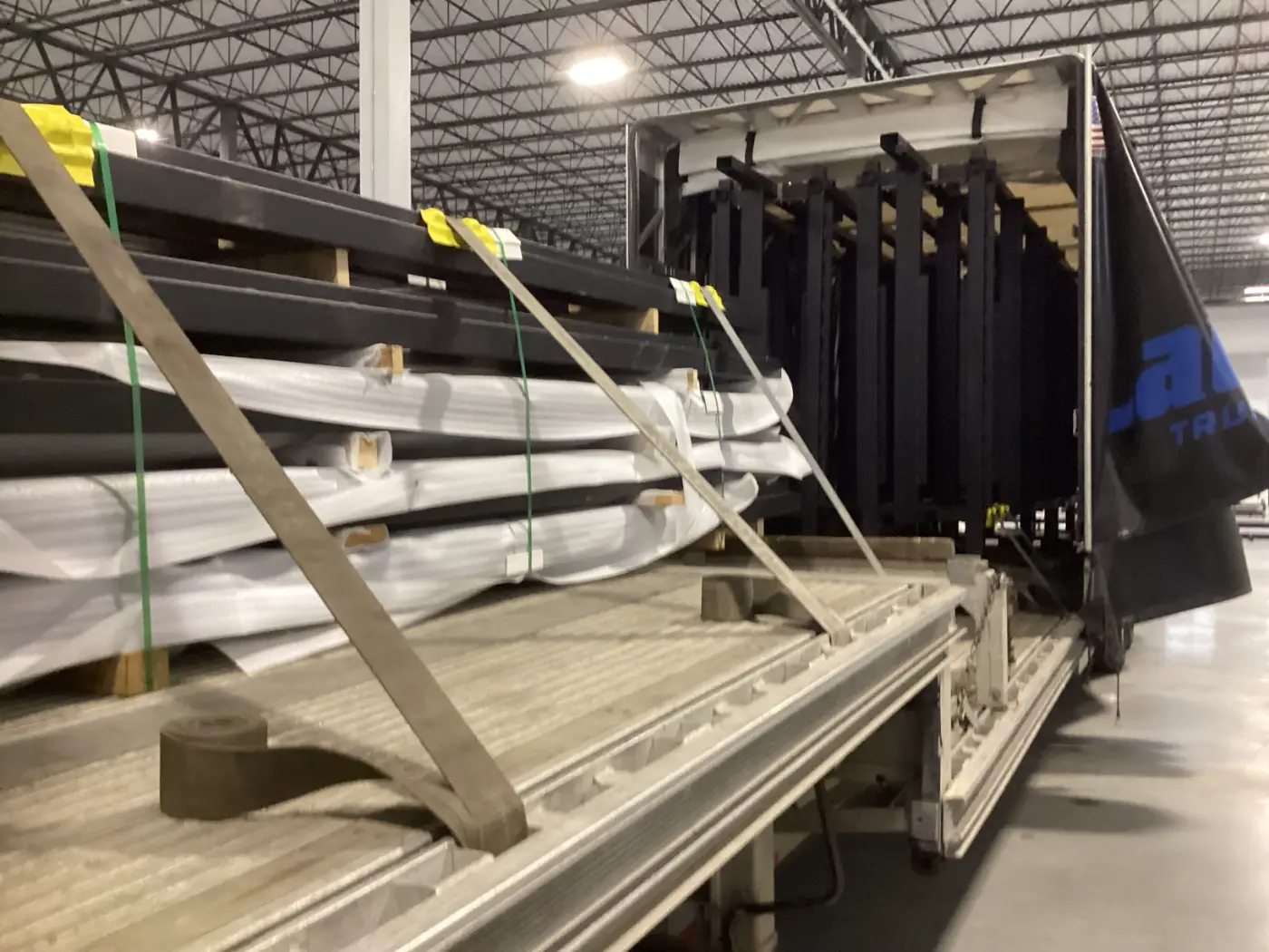 Heavy industrial machinery and equipment secured with straps on a step deck Conestoga trailer inside a Laufer Trucking warehouse.