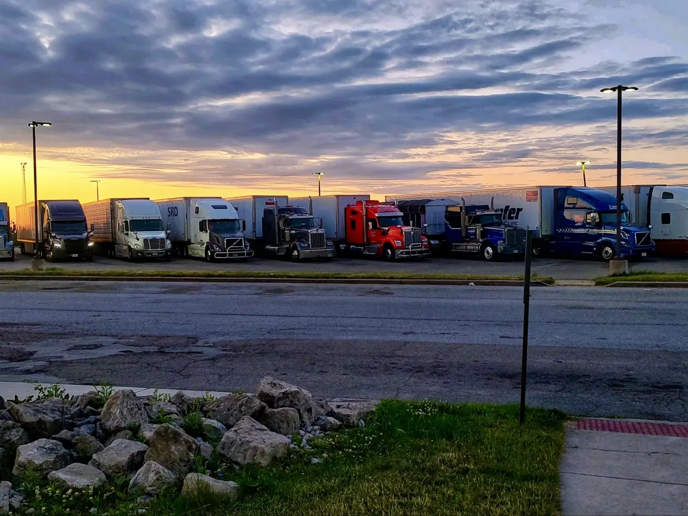 Laufer Trucking dry van and flatbed trucks lined up in a parking lot at sunset, demonstrating FCFS arrival for freight loading.