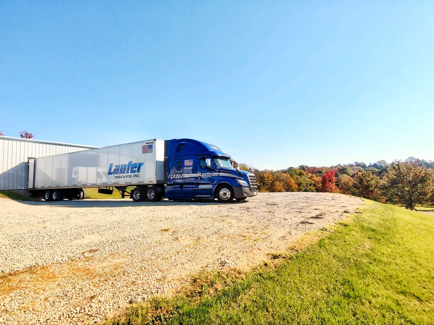 A Laufer Trucking blue semi-truck with a white dry van trailer parked at a loading dock for regional freight delivery.