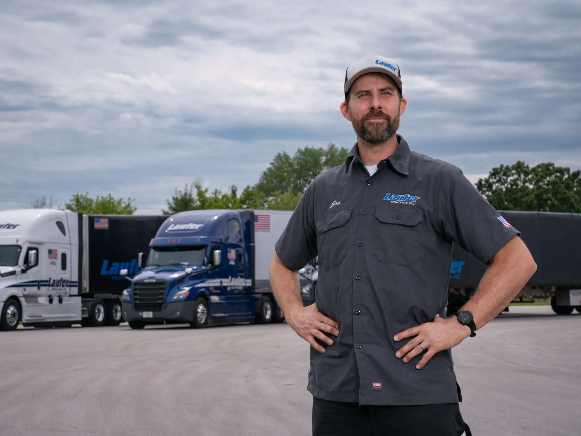 A professional Laufer Trucking driver stands in front of a fleet of semi-trucks representing family-owned freight services since 1976.