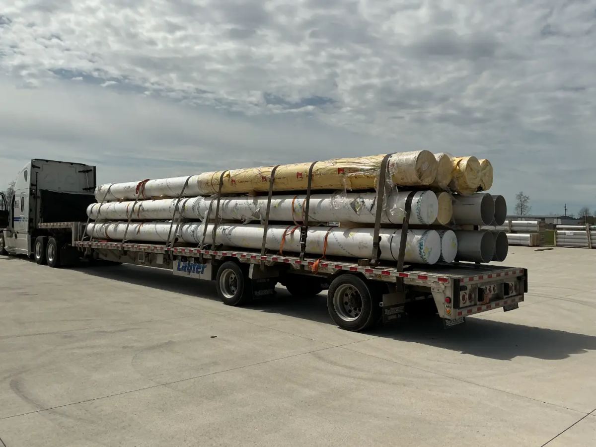 A Laufer step deck trailer loaded with large industrial pipes and freight secured by heavy-duty straps.
