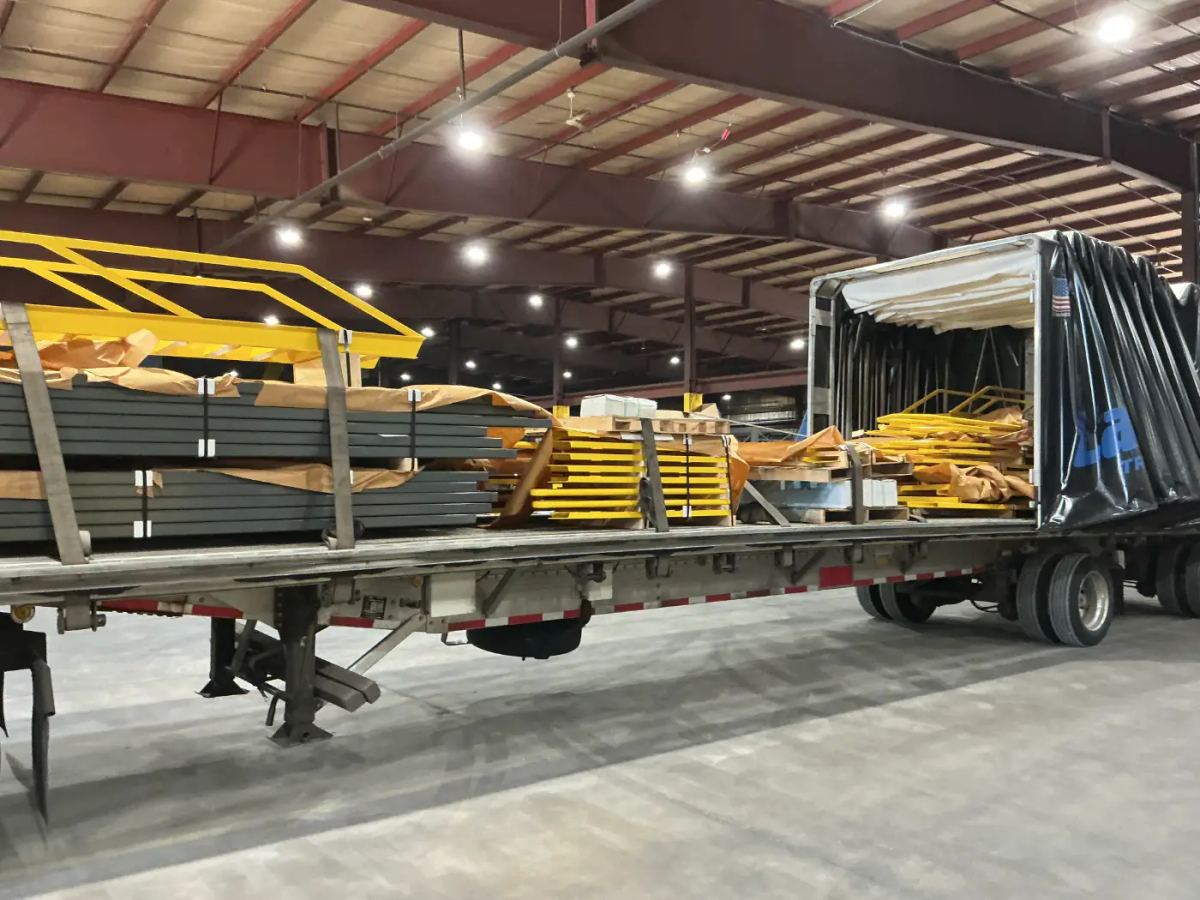 A stacked load of industrial metal components secured on a Laufer Trucking Conestoga curtain-side trailer inside a warehouse.