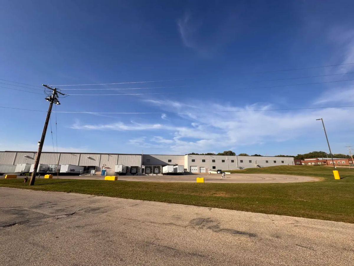 Semi-truck trailers parked at the loading docks of a large, full service Wacker Drive Logistics & Warehousing facility under a clear blue sky.