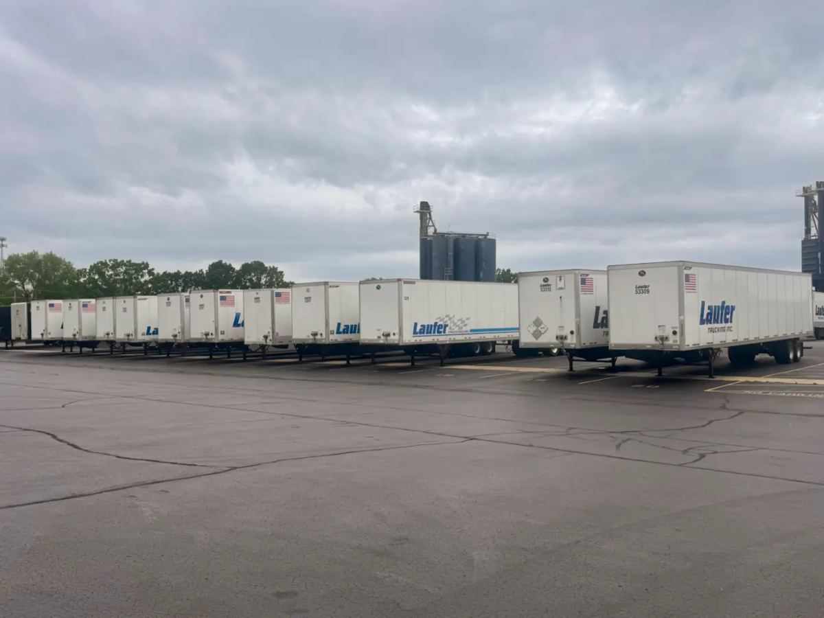 A row of Laufer Trucking white storage trailers parked in a paved lot for convenient warehousing and freight storage.
