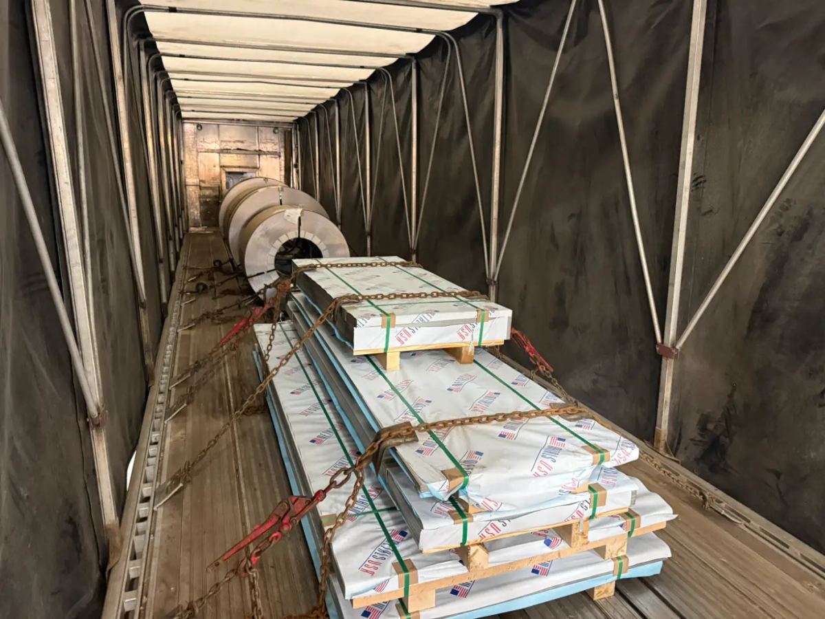 Finished steel coils and wrapped steel plates secured with chains inside a Laufer Trucking curtain-side trailer.