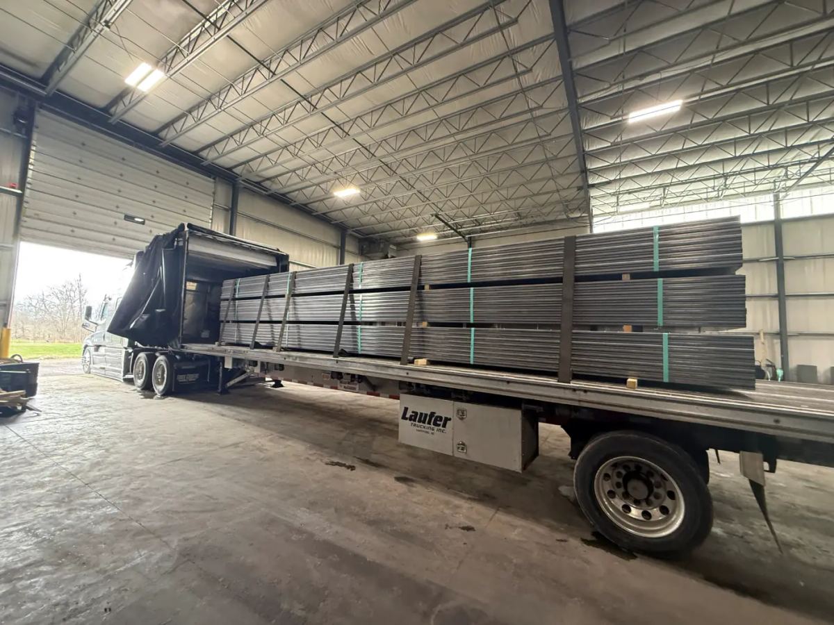 A Laufer Trucking semi-truck with a curtain-side trailer parked in a warehouse, loaded with bundled manufactured goods under cover.