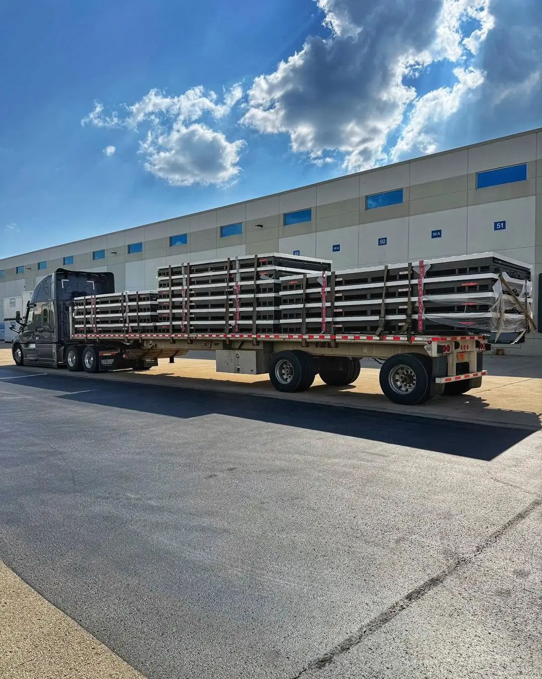 A Laufer open flatbed trailer loaded with stacked industrial cargo parked outside a commercial warehouse.