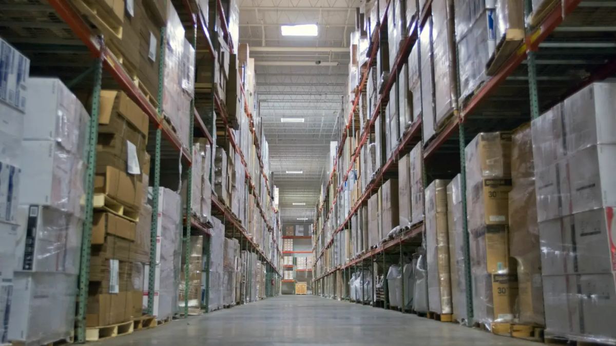 Stacked pallets of shrink-wrapped freight in a clean commercial warehouse aisle used for overflow and staging products.