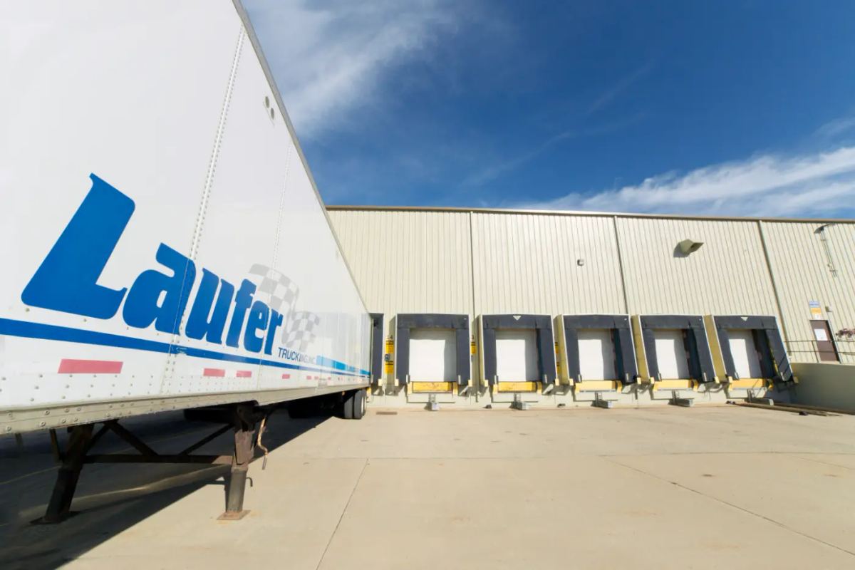 A Laufer Trucking dry van semi-trailer backed into a loading dock door for integrated warehousing and freight logistics.